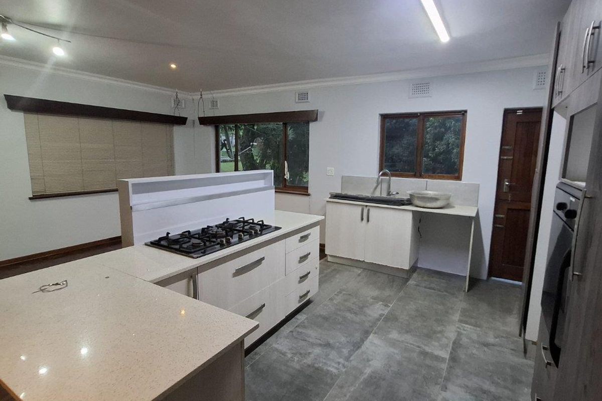 Modern kitchen featuring a central island with a gas hob, stone countertops, built-in oven, and ample cabinetry, finished with large format floor tiles.