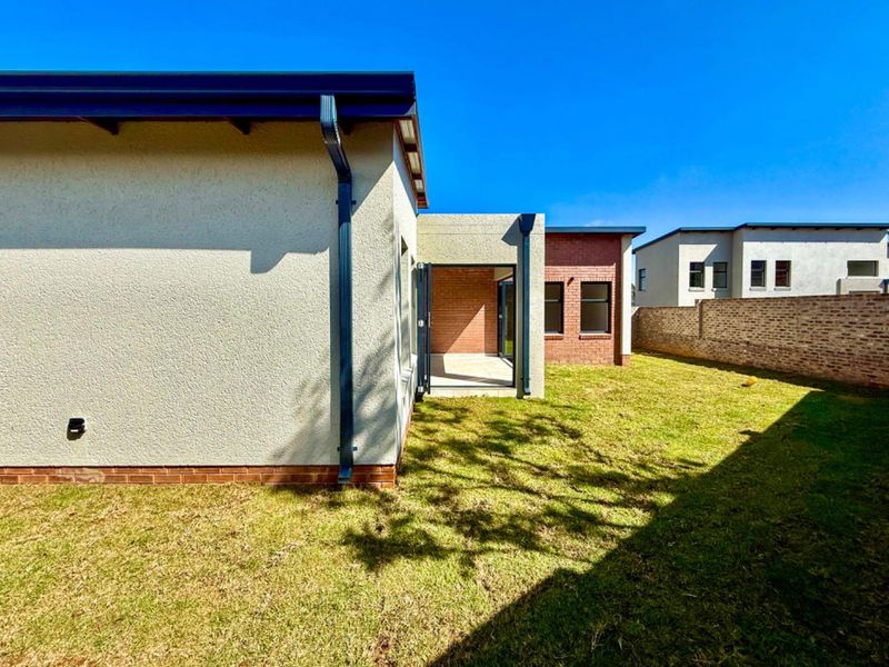 Rear view of the cluster property featuring a private garden, lawn area, and a covered patio space with modern brick and plaster finishes.