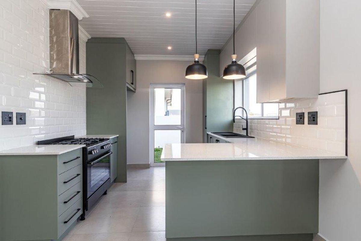 Modern kitchen featuring sage green cabinetry, white subway tile backsplash, quartz countertops, gas stove, and integrated extractor fan with a clean, contemporary finish.