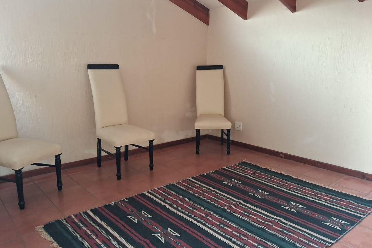 A simple living area featuring exposed timber ceiling beams, tiled flooring, and plain walls, offering a blank canvas for interior design.