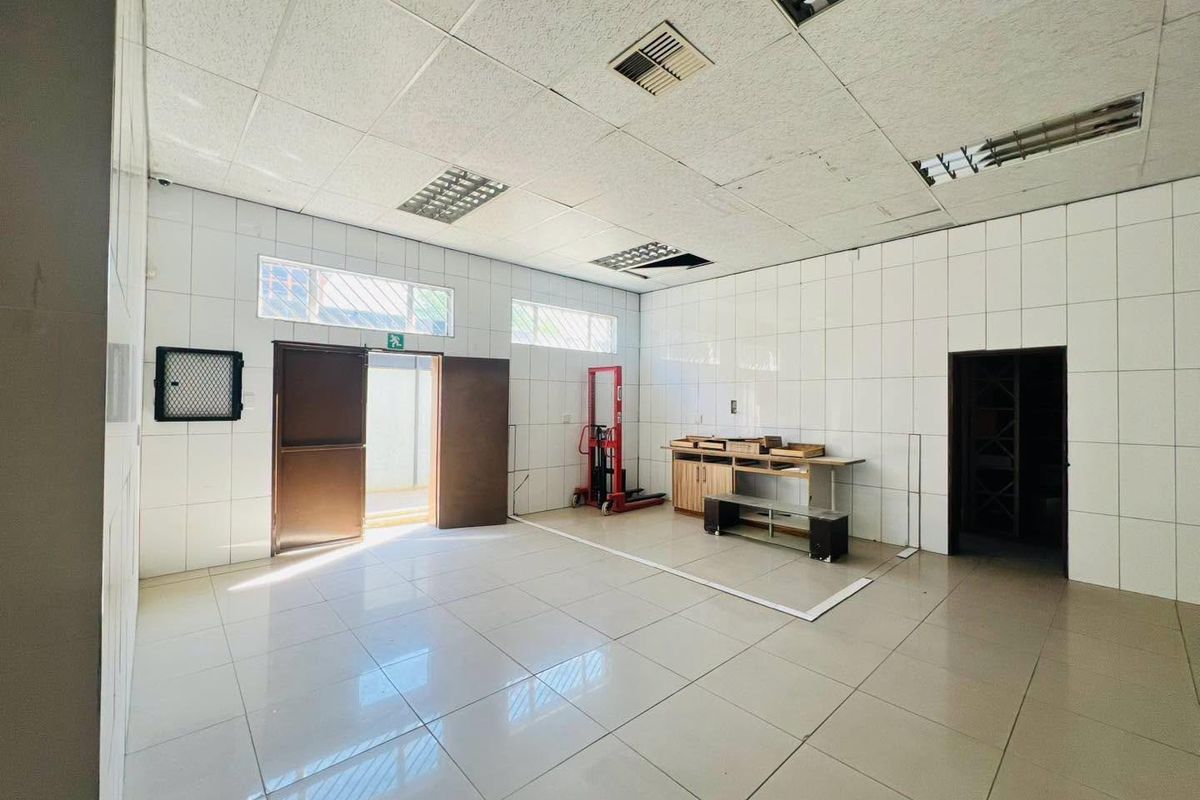 A functional utility or storage space featuring tiled walls and flooring, a suspended ceiling with recessed lighting, and direct exterior access.