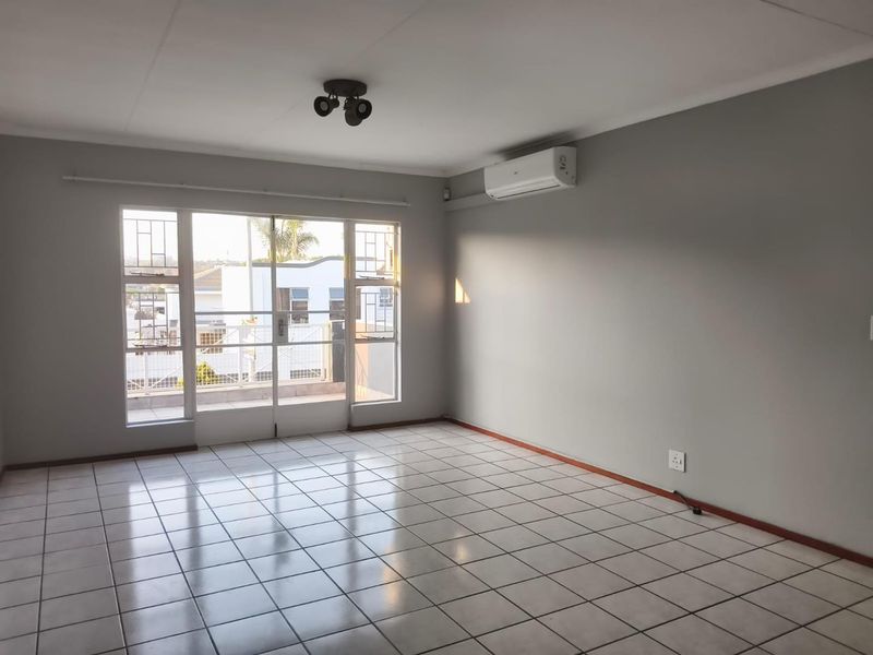 A bright, empty living room featuring tiled flooring, a wall-mounted air conditioning unit, and a sliding glass door leading to an outdoor area.