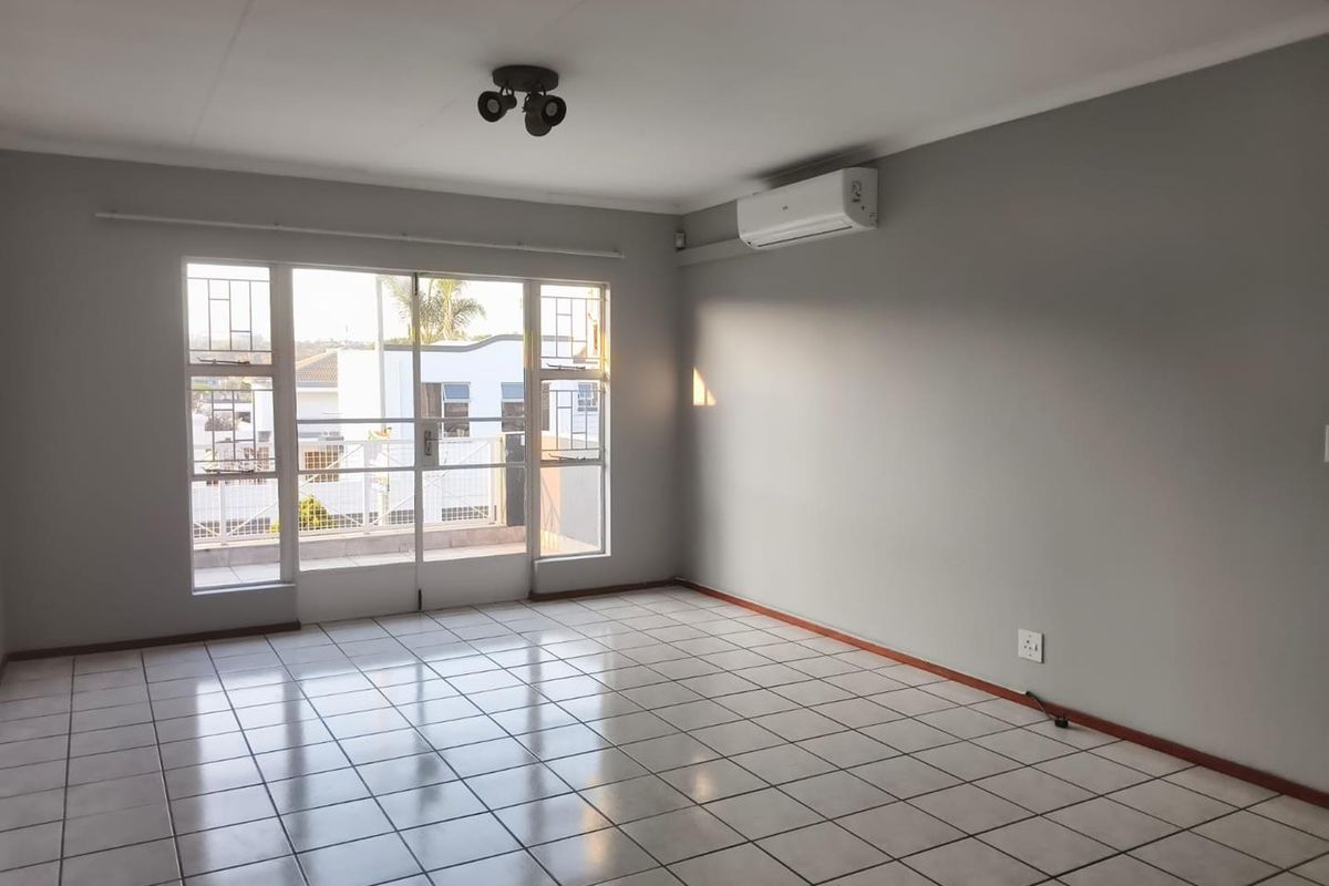 A bright, empty living room featuring tiled flooring, a wall-mounted air conditioning unit, and a sliding glass door leading to an outdoor area.