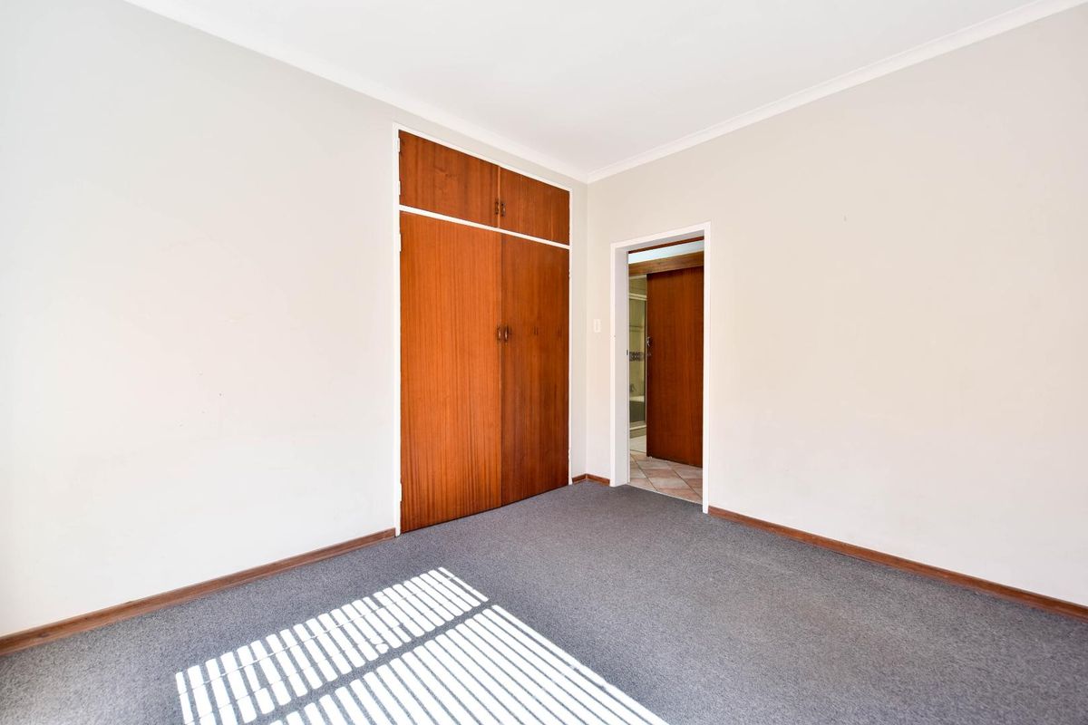 An empty bedroom featuring neutral walls, carpeted flooring, and a built-in wooden wardrobe with overhead storage.