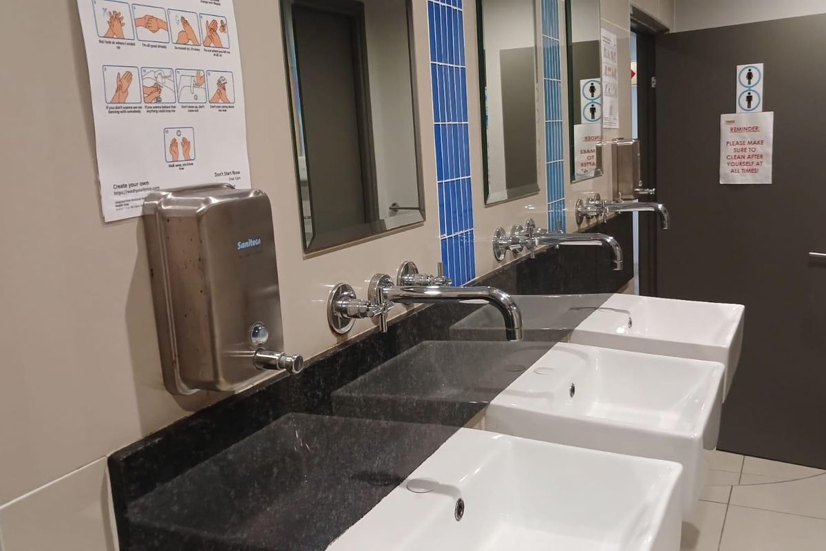A commercial-style bathroom featuring a triple vanity with granite countertops, wall-mounted chrome faucets, and integrated ceramic basins.