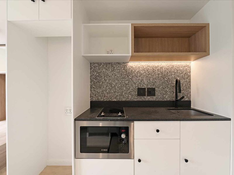 Modern compact kitchen featuring built-in microwave, electric cooktop, integrated sink, and stylish terrazzo backsplash with under-cabinet lighting.