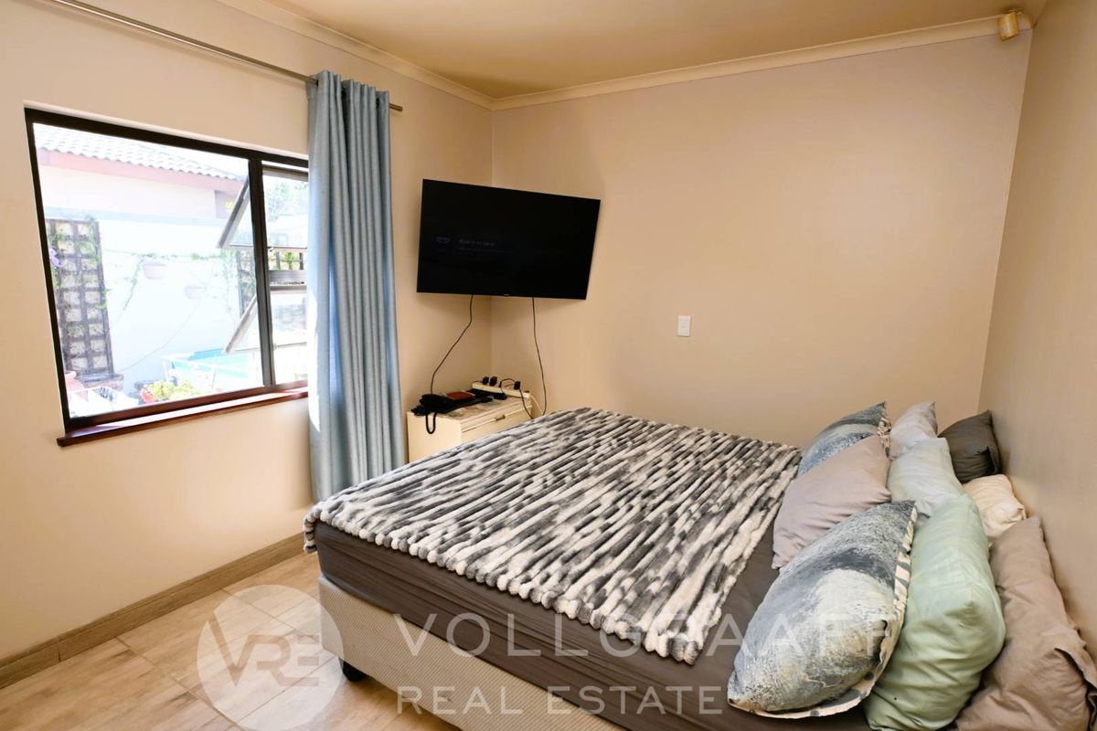 A functional bedroom featuring tiled flooring, a window with curtain rails, and a wall-mounted television.