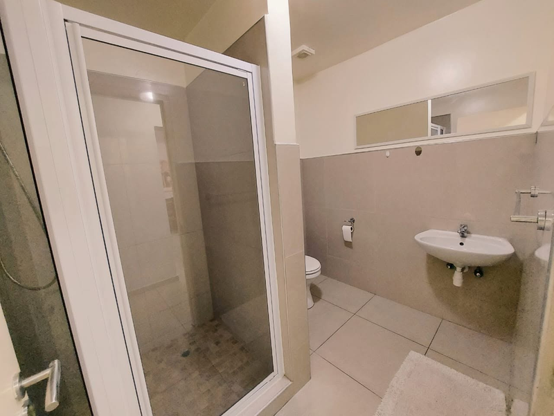 A clean, functional bathroom featuring a glass-enclosed shower, wall-mounted basin, and neutral tiled finishes throughout.