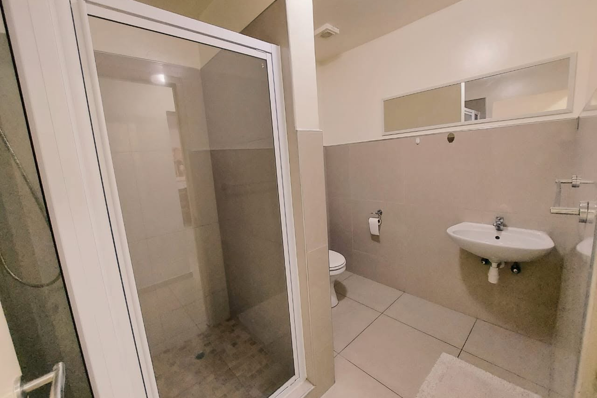 A clean, functional bathroom featuring a glass-enclosed shower, wall-mounted basin, and neutral tiled finishes throughout.