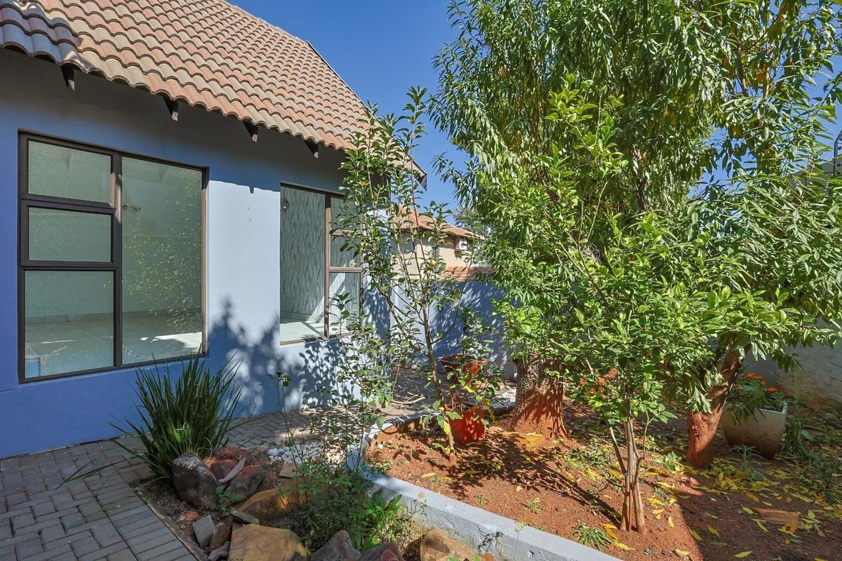 A view of the rear garden featuring a paved walkway, established trees, and a landscaped garden bed adjacent to the house exterior.