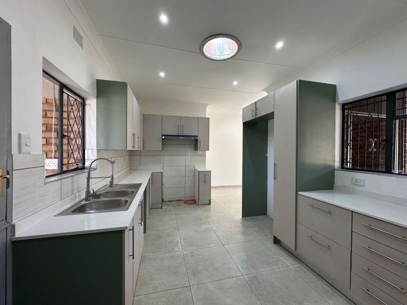Modern kitchen featuring two-tone cabinetry, double stainless steel sink, tiled flooring, and ample storage space with integrated extractor fan and natural light.