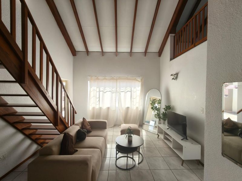 Spacious living room featuring high vaulted ceilings with exposed timber beams, a wooden staircase, and tiled flooring, offering a bright and open atmosphere.