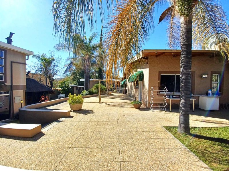 A spacious paved rear patio area featuring a retaining wall, mature palm trees, and direct access to the house via sliding doors.