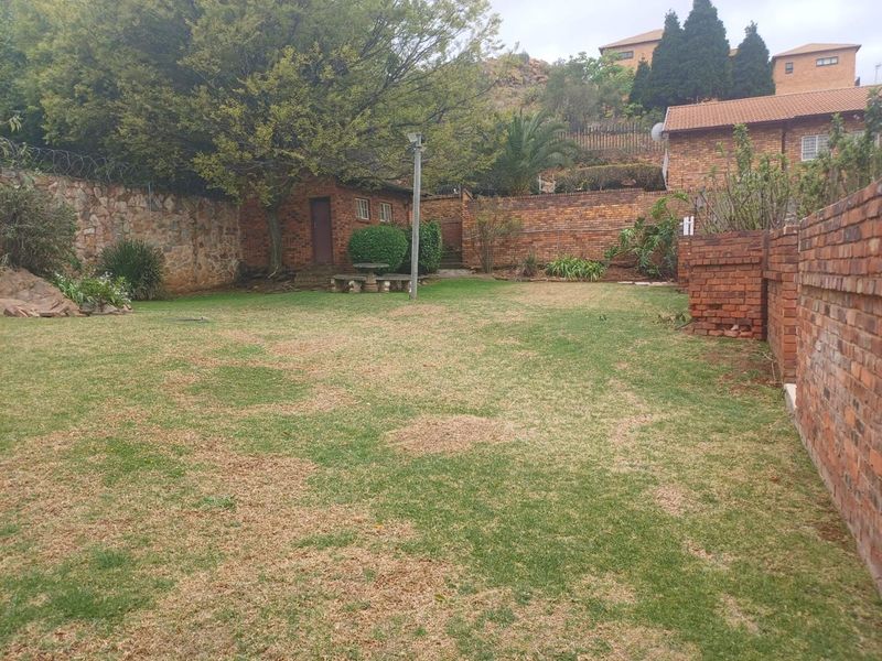 A spacious private garden featuring established trees, brick boundary walls with security fencing, and a small brick outbuilding.