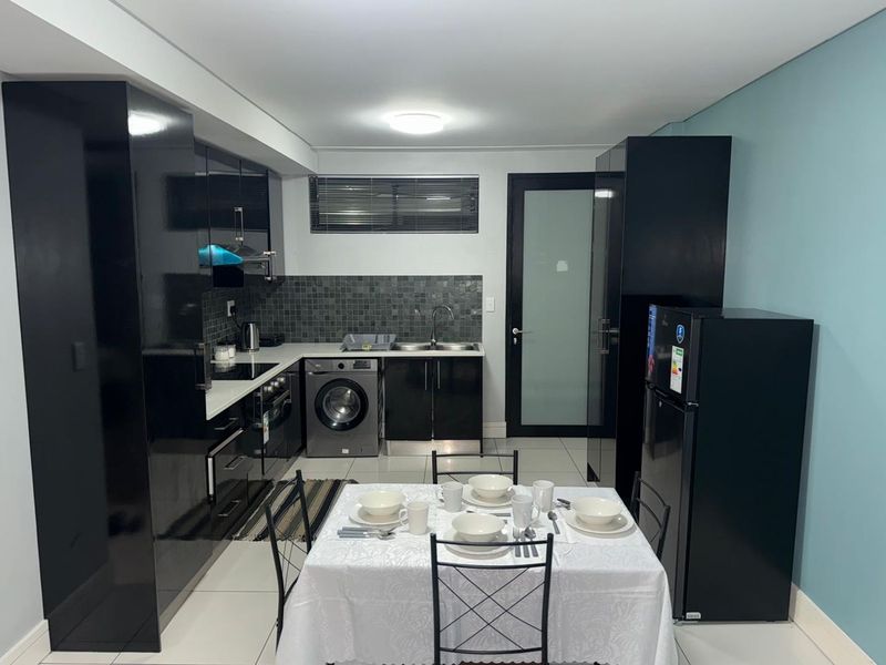 Modern open-plan kitchen and dining area featuring sleek black cabinetry, integrated appliances, tiled flooring, and a functional layout.