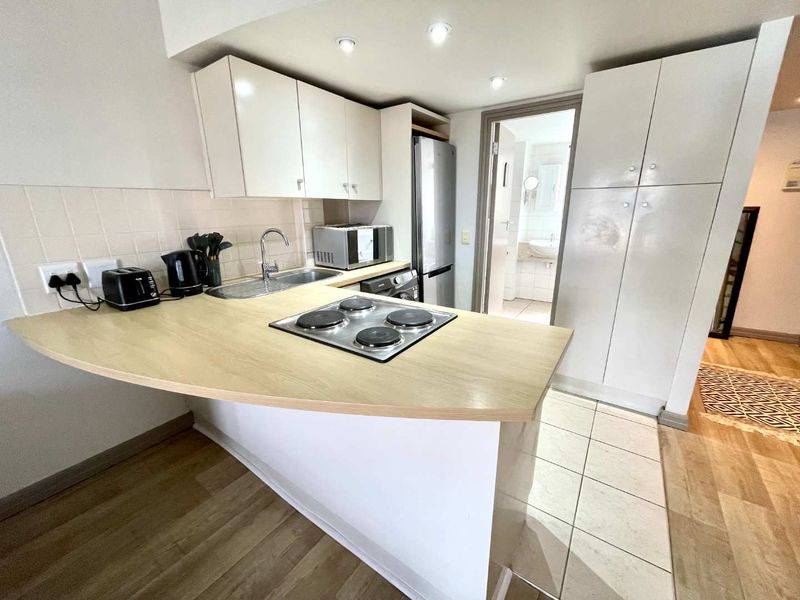 Compact kitchen featuring white built-in cabinetry, a light wood-tone countertop with an integrated electric hob, and a tiled backsplash.