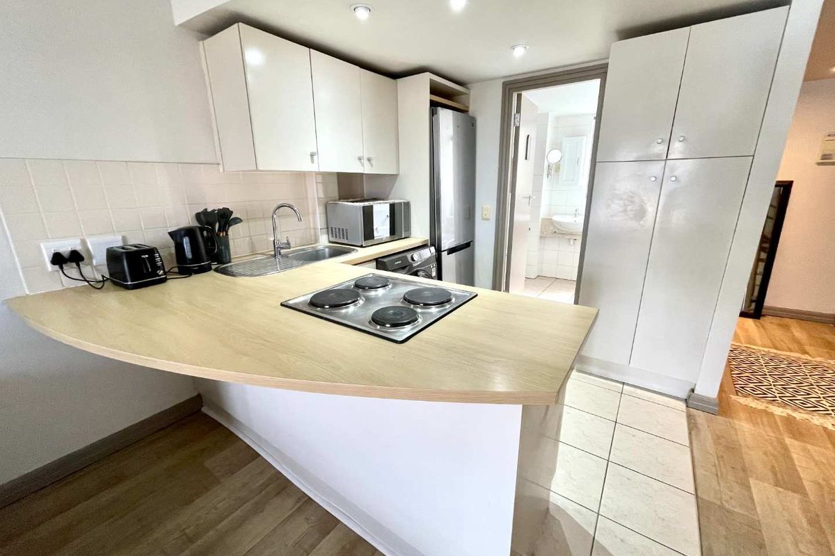 Compact kitchen featuring white built-in cabinetry, a light wood-tone countertop with an integrated electric hob, and a tiled backsplash.