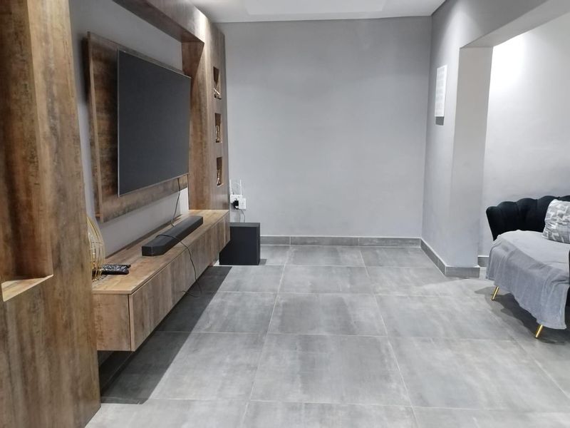 A modern living room featuring large format grey floor tiles and a custom built-in wooden media unit with integrated shelving.