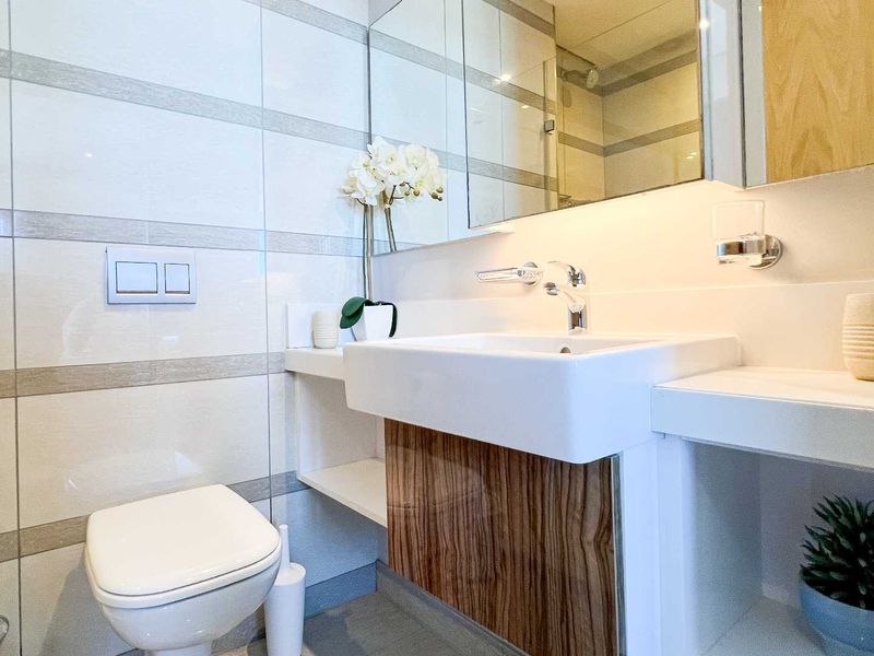 Modern bathroom featuring a wall-mounted toilet with concealed cistern, vanity basin with mixer tap, and a mirrored medicine cabinet.