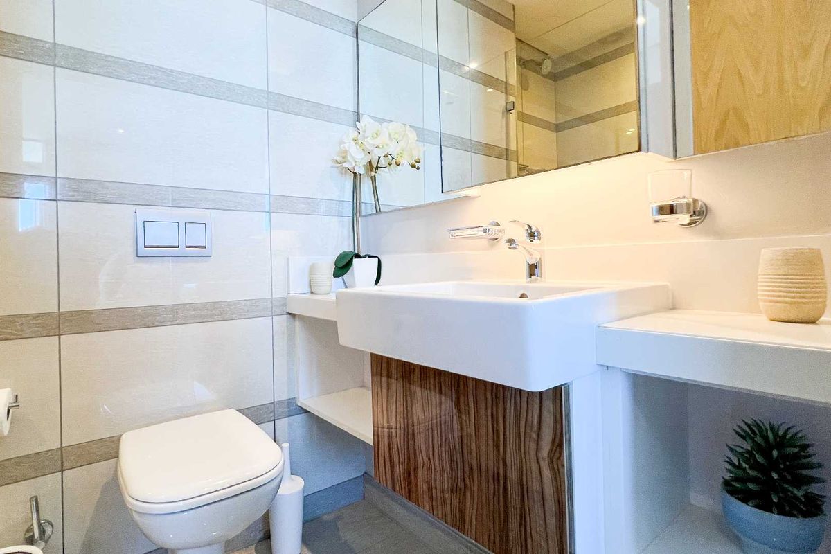 Modern bathroom featuring a wall-mounted toilet with concealed cistern, vanity basin with mixer tap, and a mirrored medicine cabinet.