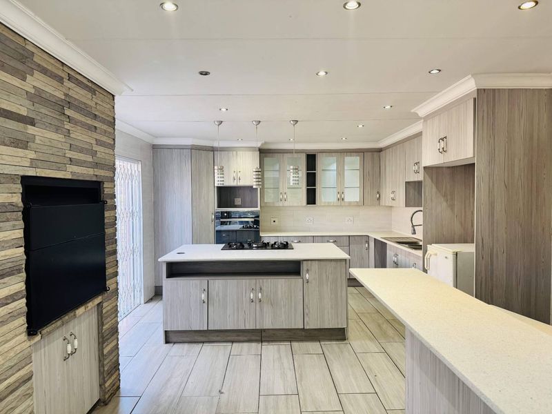 Modern kitchen featuring light wood-grain cabinetry, stone countertops, a central island with a gas hob, and an integrated stone-clad fireplace.