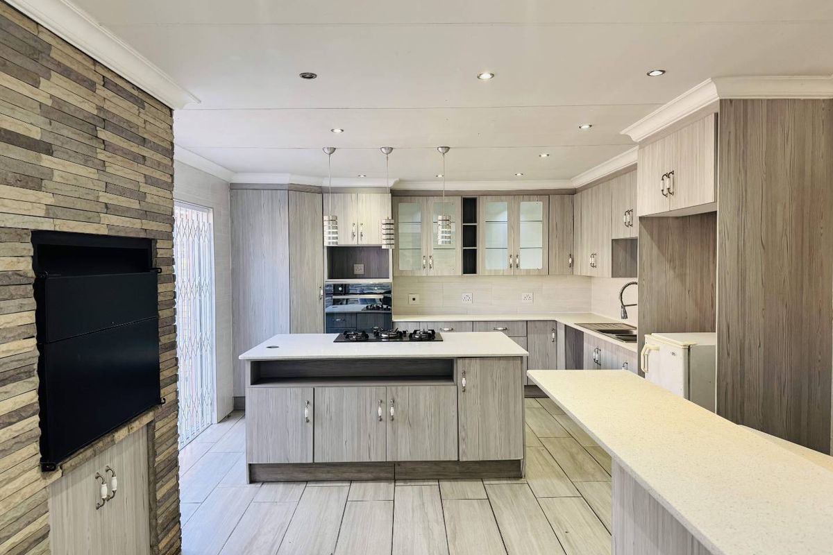 Modern kitchen featuring light wood-grain cabinetry, stone countertops, a central island with a gas hob, and an integrated stone-clad fireplace.
