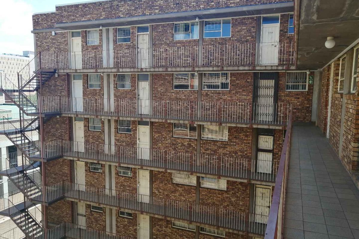 Exterior view of a multi-story apartment building featuring brick facade, external walkways, metal security gates, and steel stairwell access.