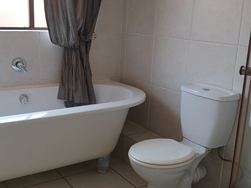 A functional bathroom featuring a freestanding bathtub, a separate shower enclosure, and a standard toilet with neutral wall and floor tiling.