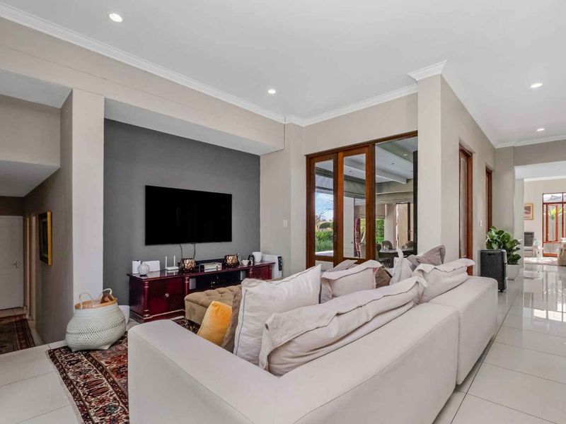 Spacious living room featuring tiled flooring, recessed lighting, and timber-framed glass doors leading to an outdoor area, creating a bright and open atmosphere.