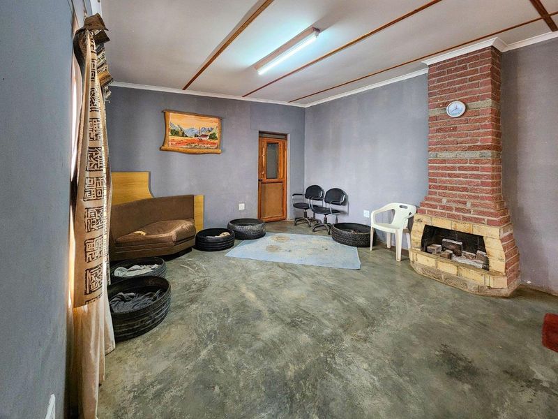 Living room featuring a prominent brick fireplace, exposed ceiling beams, and concrete flooring, offering a blank canvas for renovation and modernization.