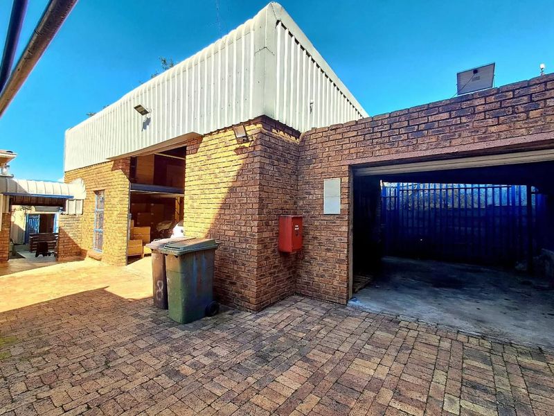Rear exterior view of a commercial property featuring face brick walls, corrugated metal cladding, and a paved courtyard area with secure access.