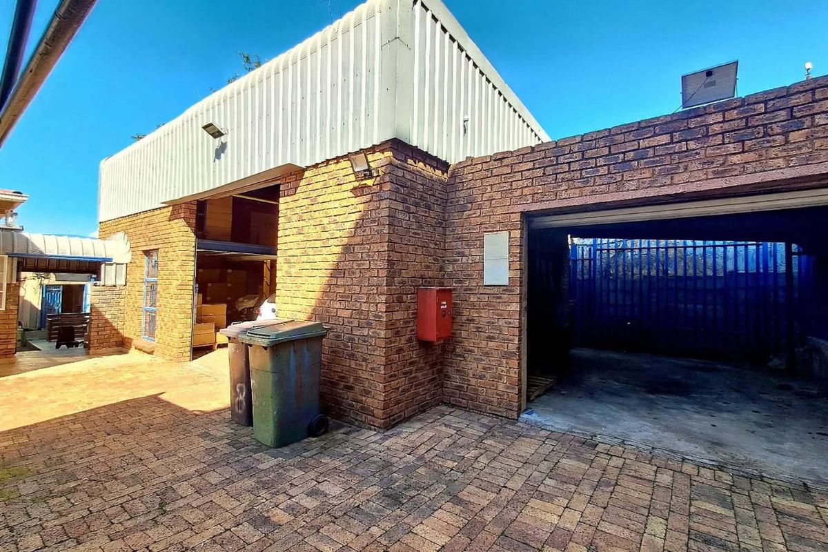 Rear exterior view of a commercial property featuring face brick walls, corrugated metal cladding, and a paved courtyard area with secure access.