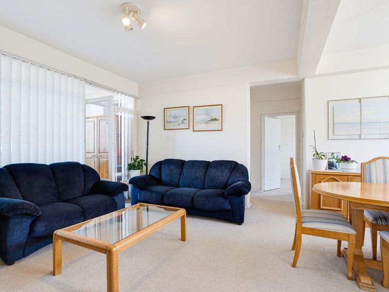Spacious open-plan living and dining area featuring neutral carpeting, vertical blinds, and access to an adjoining room.