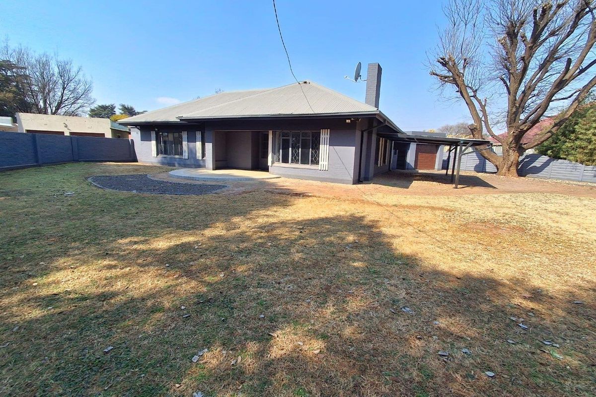 Rear view of a single-story house featuring a corrugated metal roof, a paved patio area, and a spacious backyard with perimeter walling.