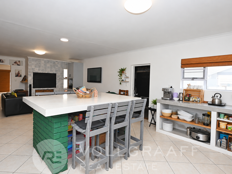 Spacious open-plan living and kitchen area featuring a central island with concrete countertop, brick base, and built-in shelving units.