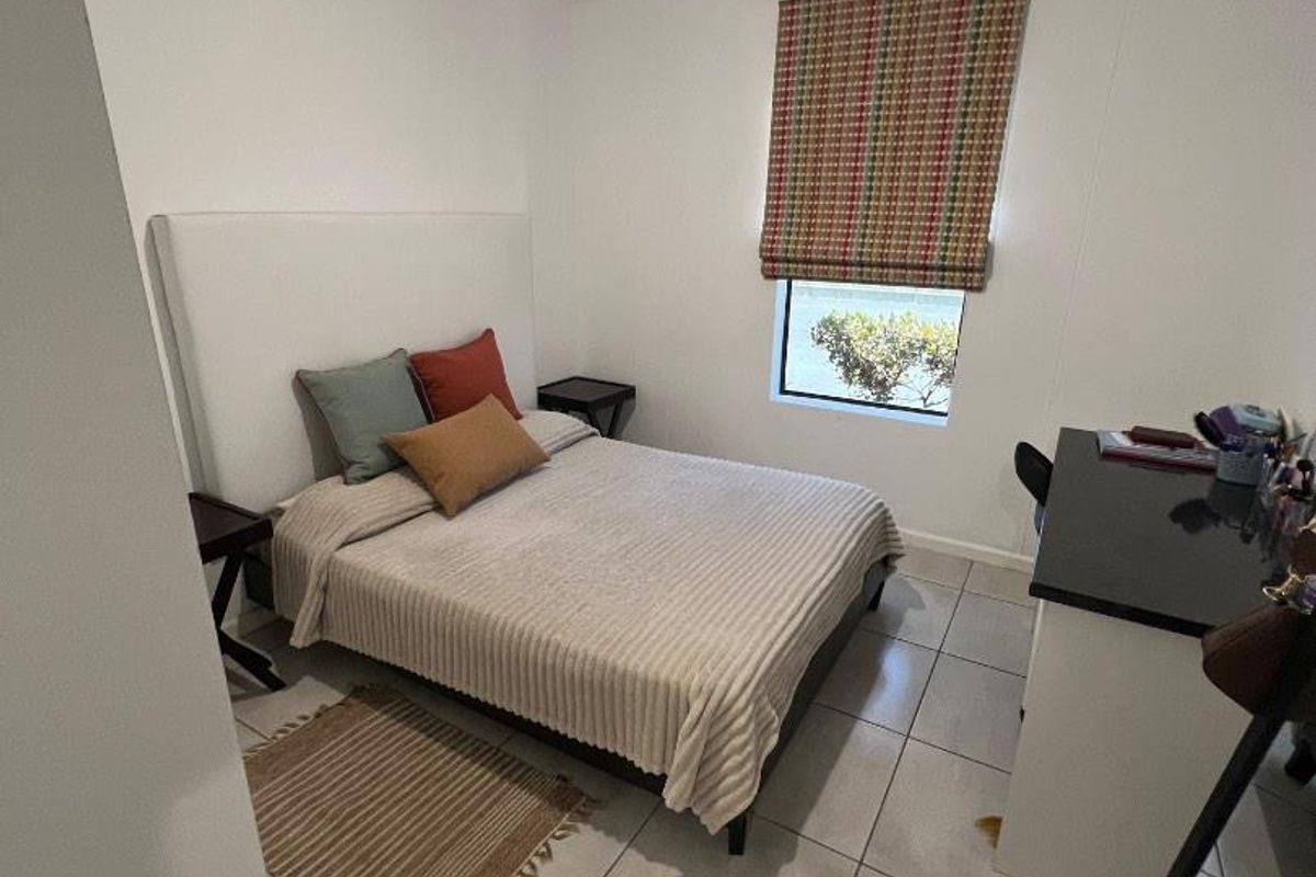 A functional bedroom featuring tiled flooring, a window with a fitted roman blind, and a simple overhead light fixture.