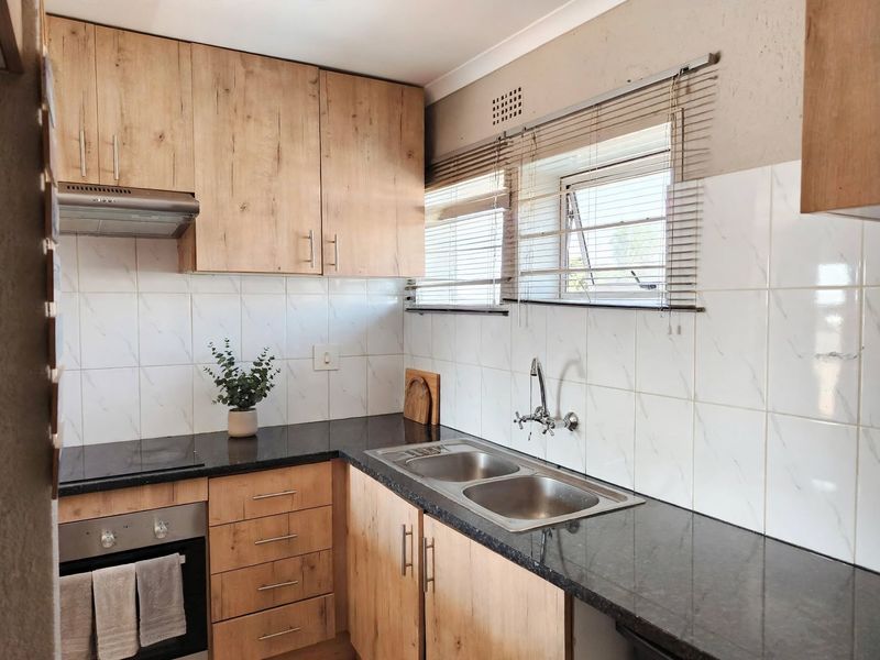 Modern kitchen featuring wood-look cabinetry, granite countertops, a double stainless steel sink, and integrated appliances including an oven and hob.