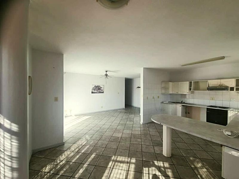Spacious open-plan living and kitchen area featuring tiled flooring, built-in cabinetry, and a breakfast counter, offering a blank canvas for renovation.
