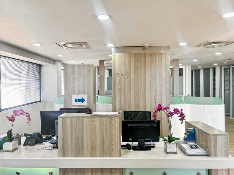 A professional office reception area featuring a modern wood-finish desk, recessed lighting, and glass partitions, creating a clean and welcoming corporate environment.