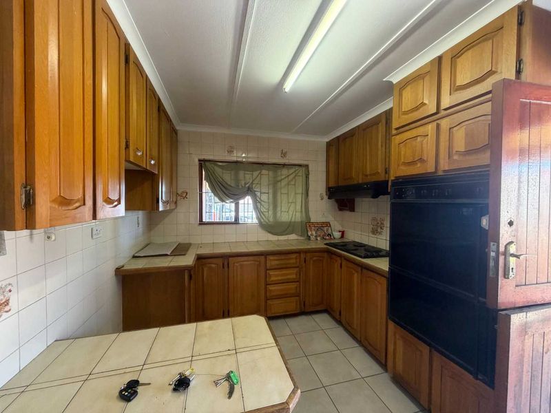 A functional kitchen featuring traditional wooden cabinetry, tiled countertops, built-in oven, and hob, offering a classic layout with ample storage space.