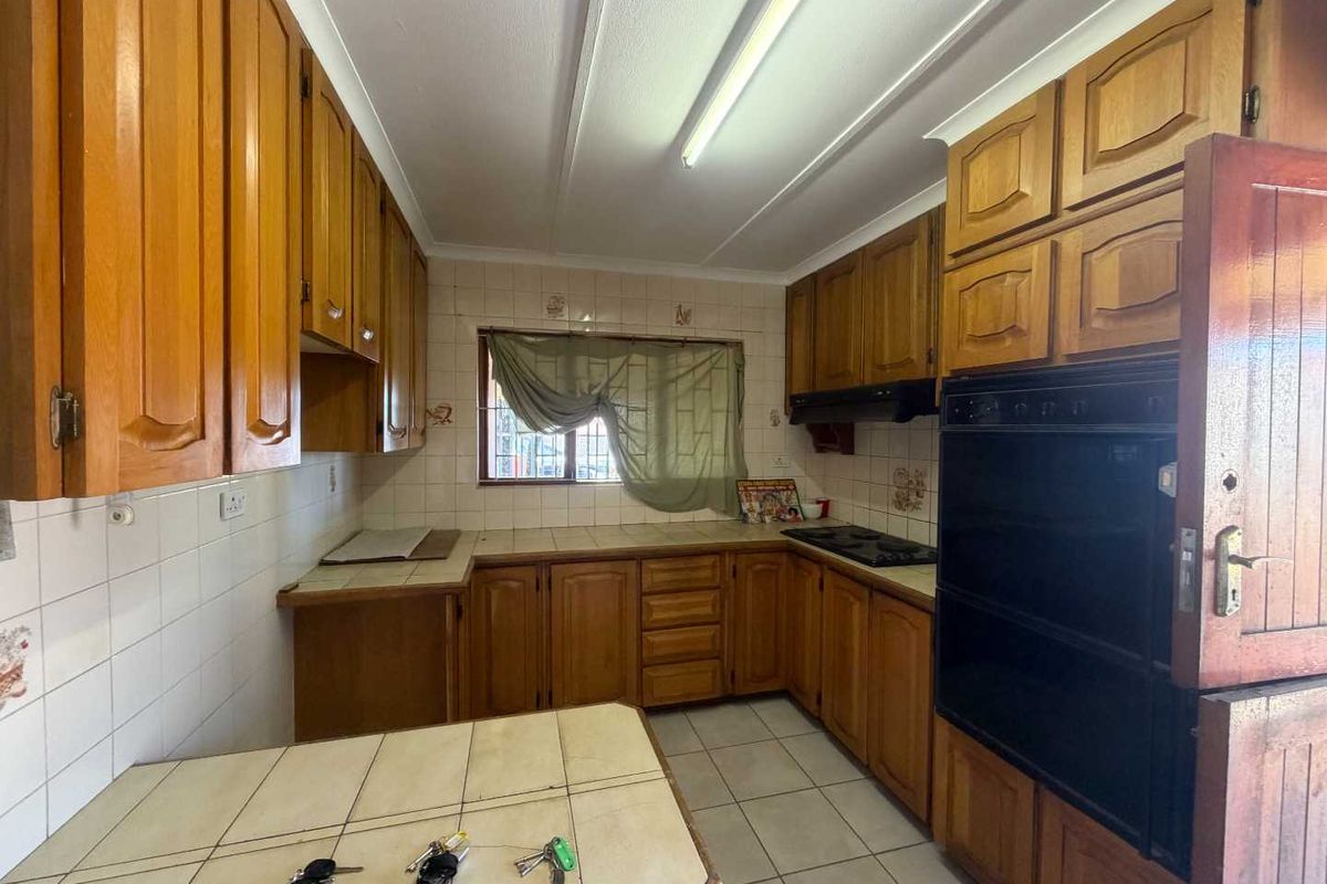 A functional kitchen featuring traditional wooden cabinetry, tiled countertops, built-in oven, and hob, offering a classic layout with ample storage space.