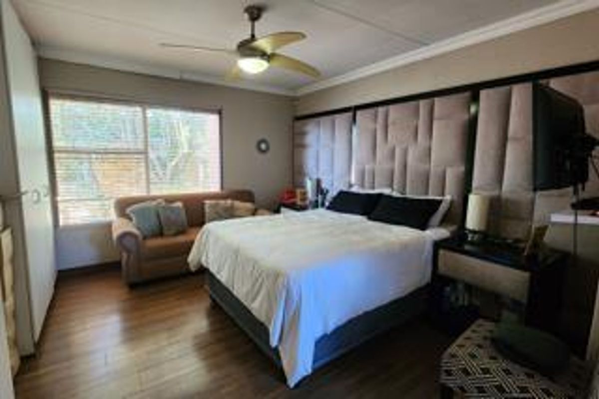 Spacious bedroom featuring laminate flooring, a ceiling fan, and a large upholstered feature wall behind the bed area.
