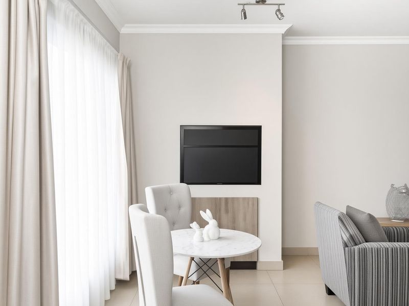 A bright living area featuring neutral walls, crown molding, tiled flooring, and a recessed wall mount for a television.