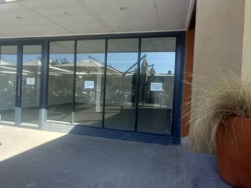 A retail storefront featuring a large glass facade, aluminum framing, and a covered paved entrance area.
