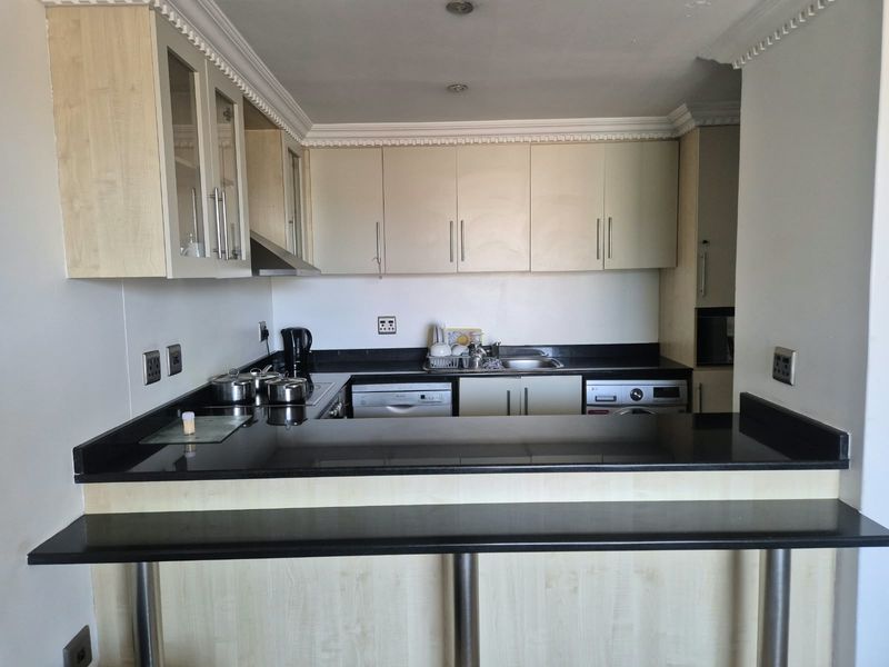 A functional kitchen featuring light wood cabinetry, black granite countertops, a breakfast bar, and integrated appliances including a dishwasher and washing machine.