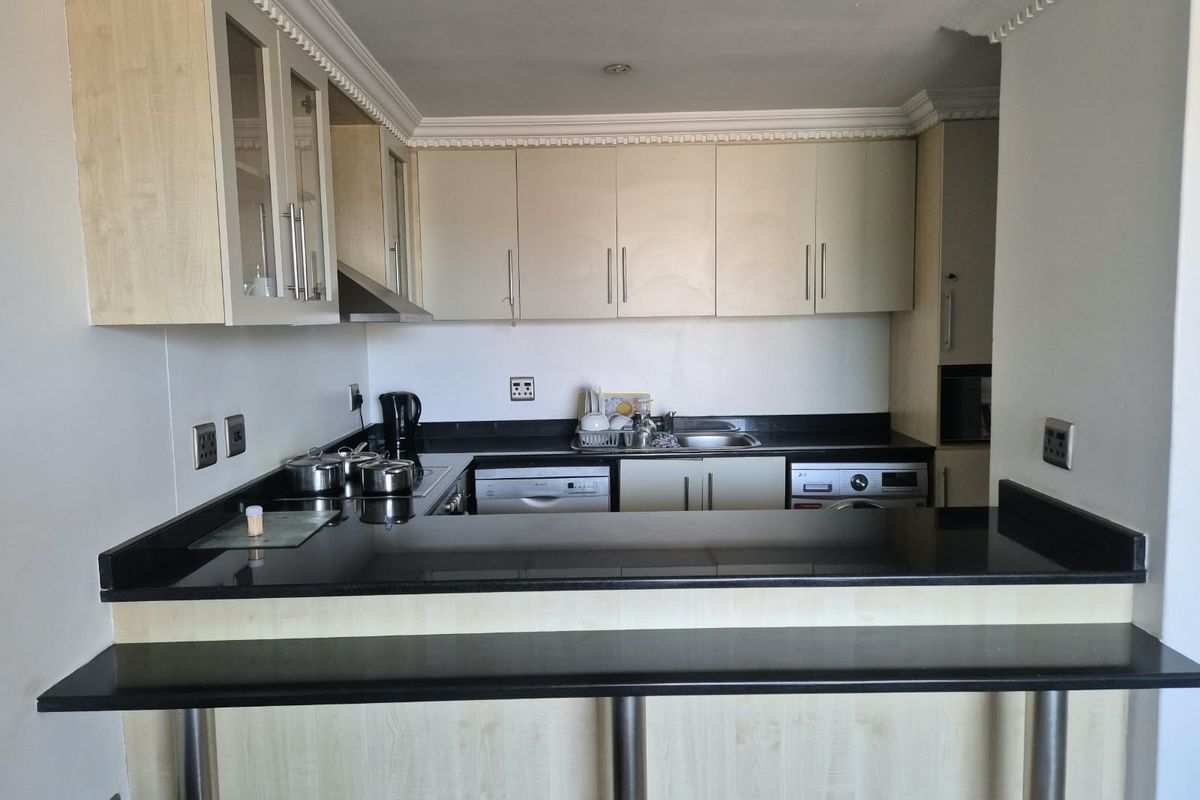 A functional kitchen featuring light wood cabinetry, black granite countertops, a breakfast bar, and integrated appliances including a dishwasher and washing machine.