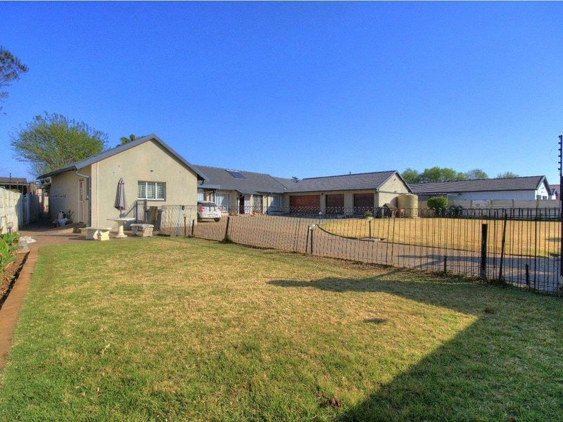 Spacious rear garden area featuring a paved driveway, lawn, and perimeter fencing with integrated electric security.