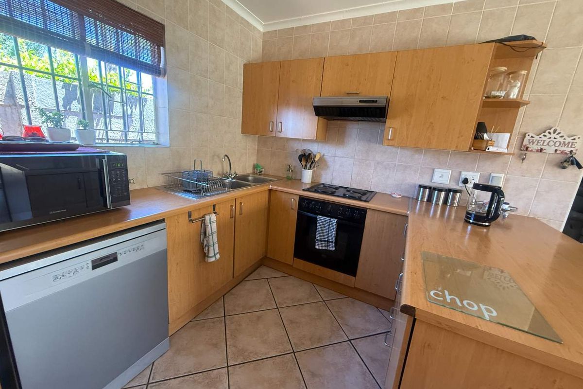 A functional kitchen featuring light wood cabinetry, laminate countertops, a built-in oven with gas hob, and tiled finishes throughout.