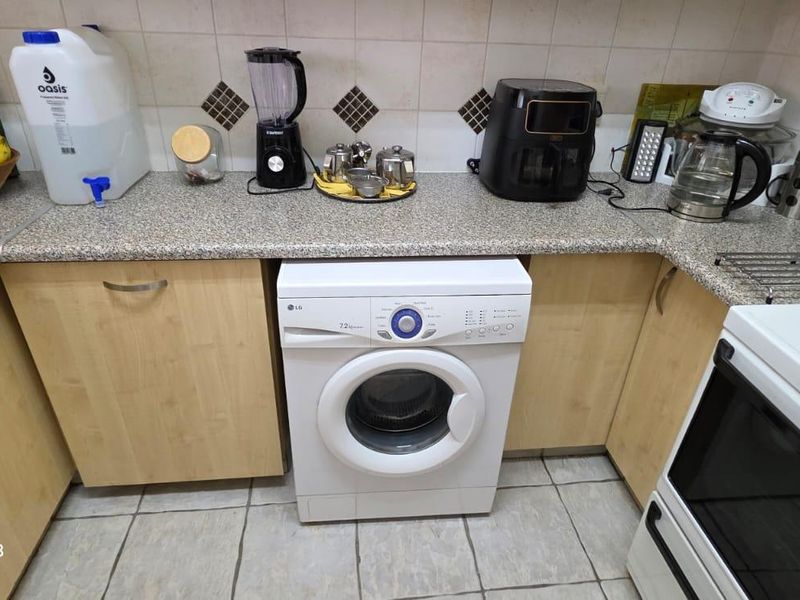 A functional kitchen featuring laminate cabinetry, granite-look countertops, ceramic tile backsplash, and integrated space for a washing machine.