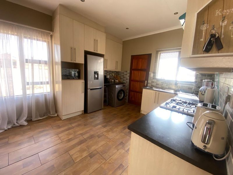 A functional kitchen featuring light wood-finish cabinetry, dark countertops, a gas hob, and wood-look floor tiles with ample natural light.
